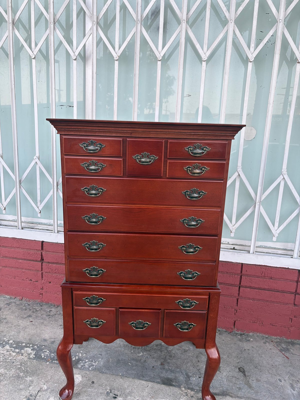 Tall red wooden dresser with brass handles on wheels against a white latticed gate and pink painted wall