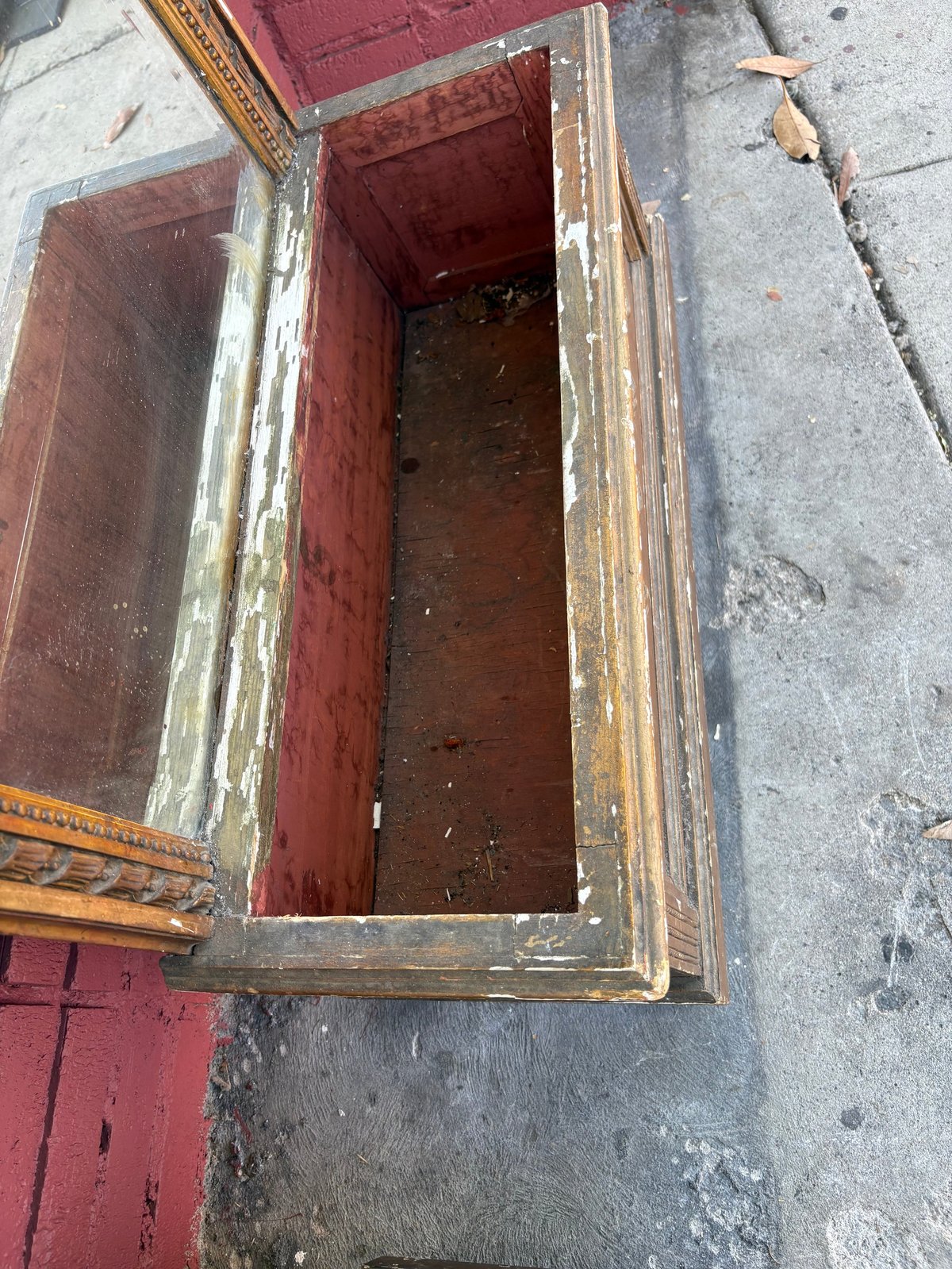 Open wooden storage chest or trunk with red interior and weathered wooden frame sitting on concrete ground
