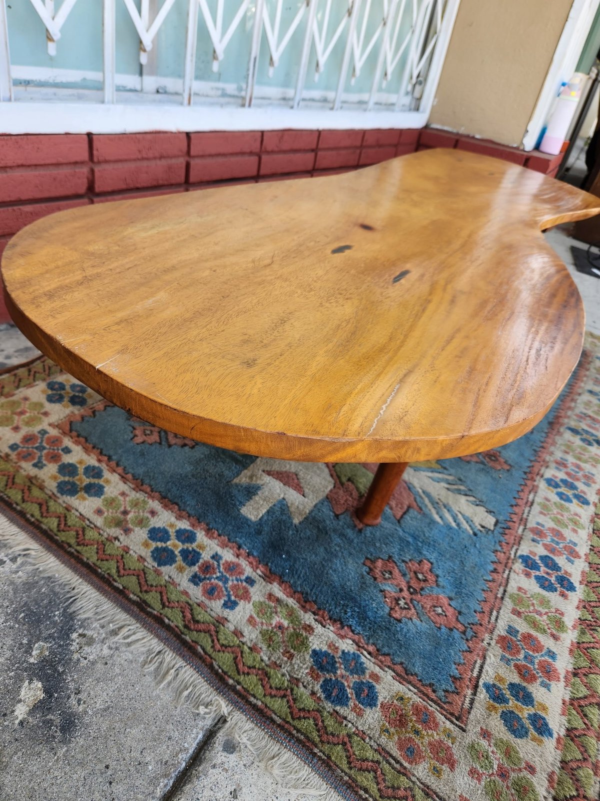 Large oval wooden dining table with natural finish on colorful area rug, red cushioned seating in background