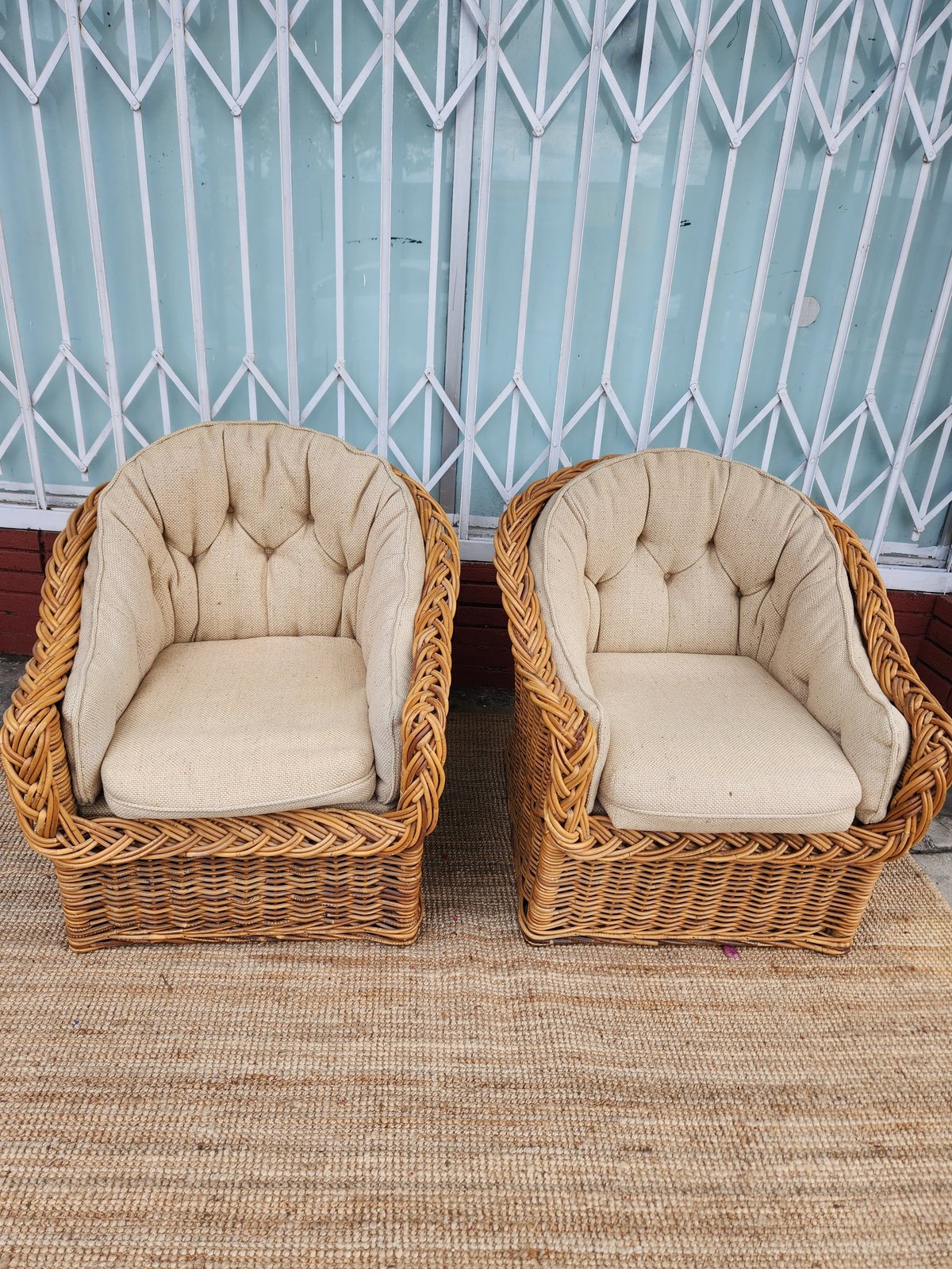 Pair of woven wicker armchairs with cream-colored cushioned seating against a blue lattice wall