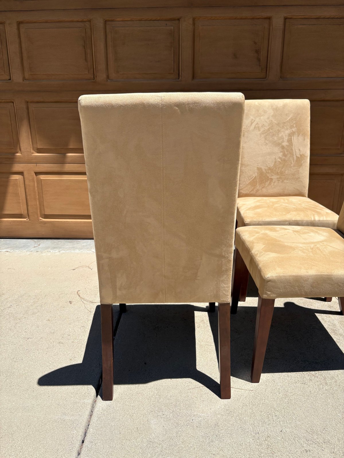 Rear view of beige upholstered dining chairs with wooden legs displayed outdoors against a wooden paneled wall