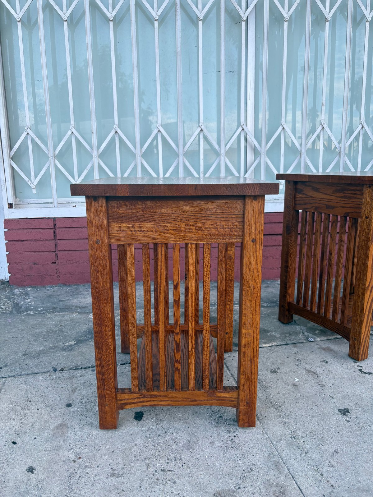 Wooden side table with vertical slat detailing displayed outdoors against metal security gate and maroon wall