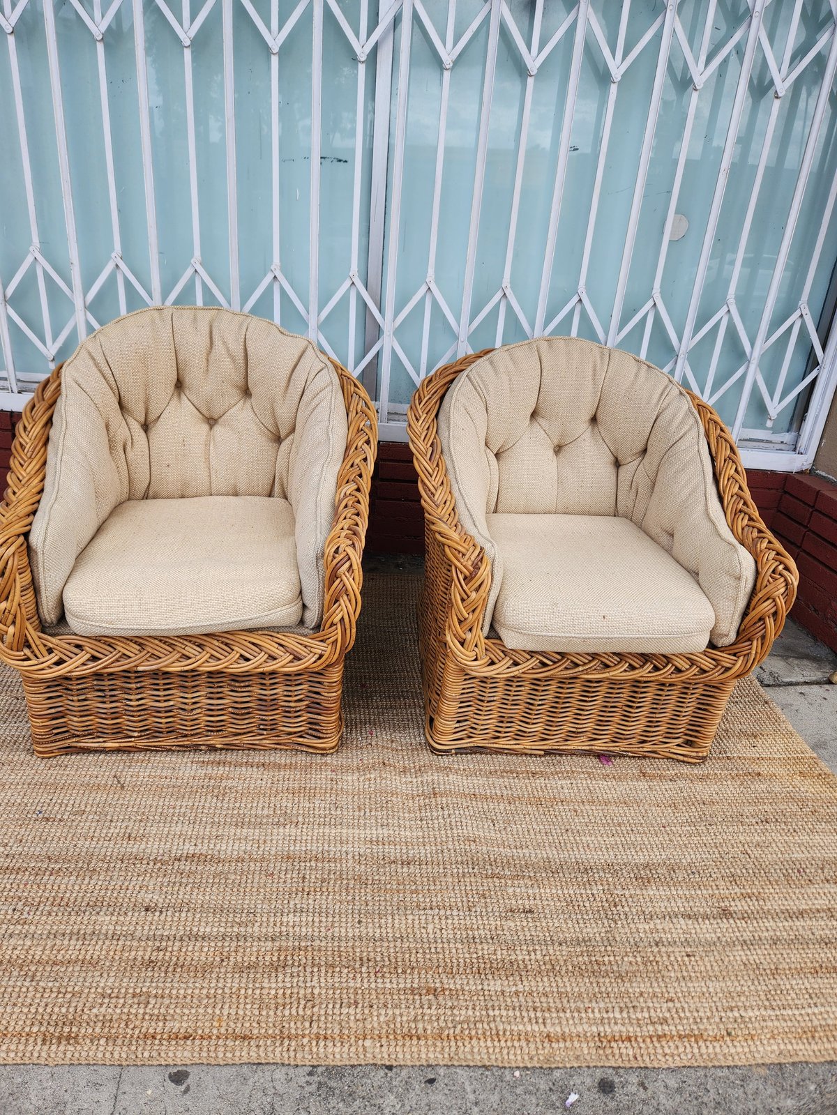 Pair of wicker armchairs with beige cushions on a tan rug against a blue and white striped wall