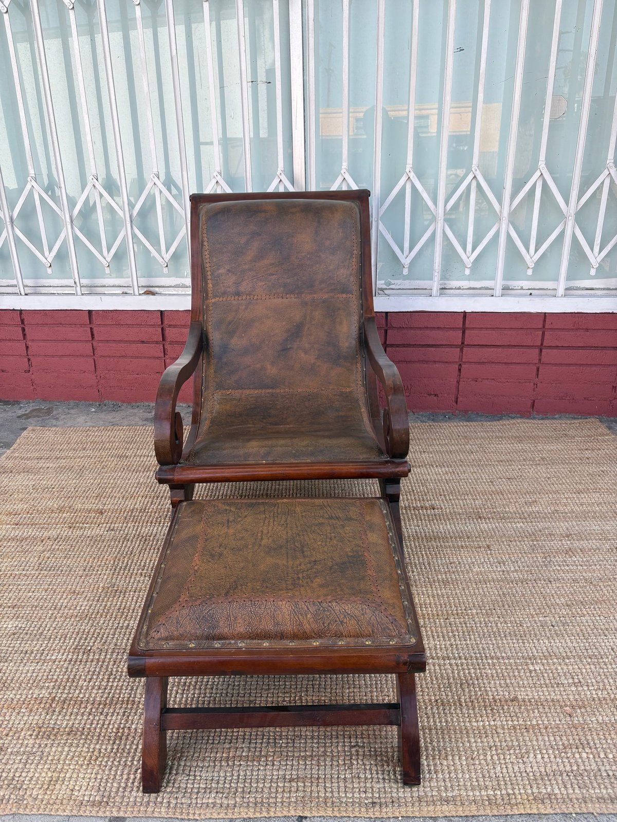 Vintage leather lounge chair with matching ottoman on woven rug against red and white building wall