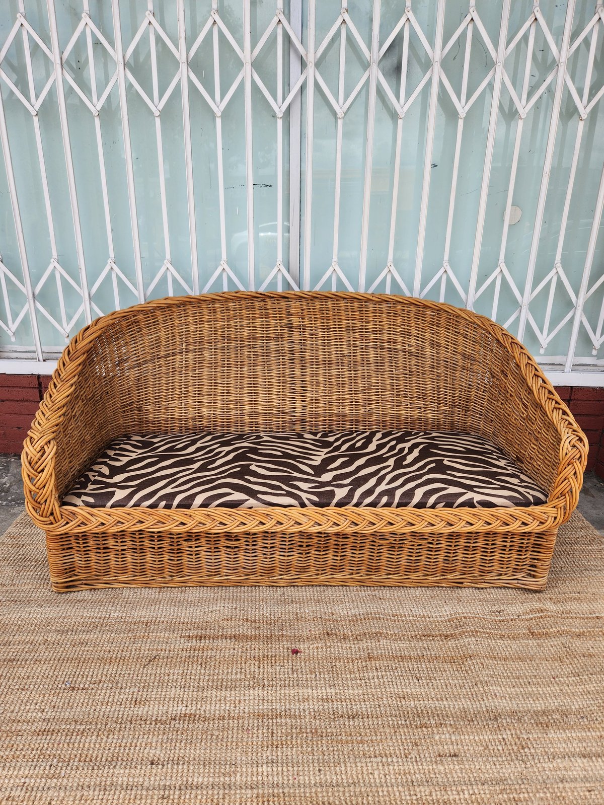 Wicker pet bed with zebra-print cushion in front of a white accordion-style metal gate