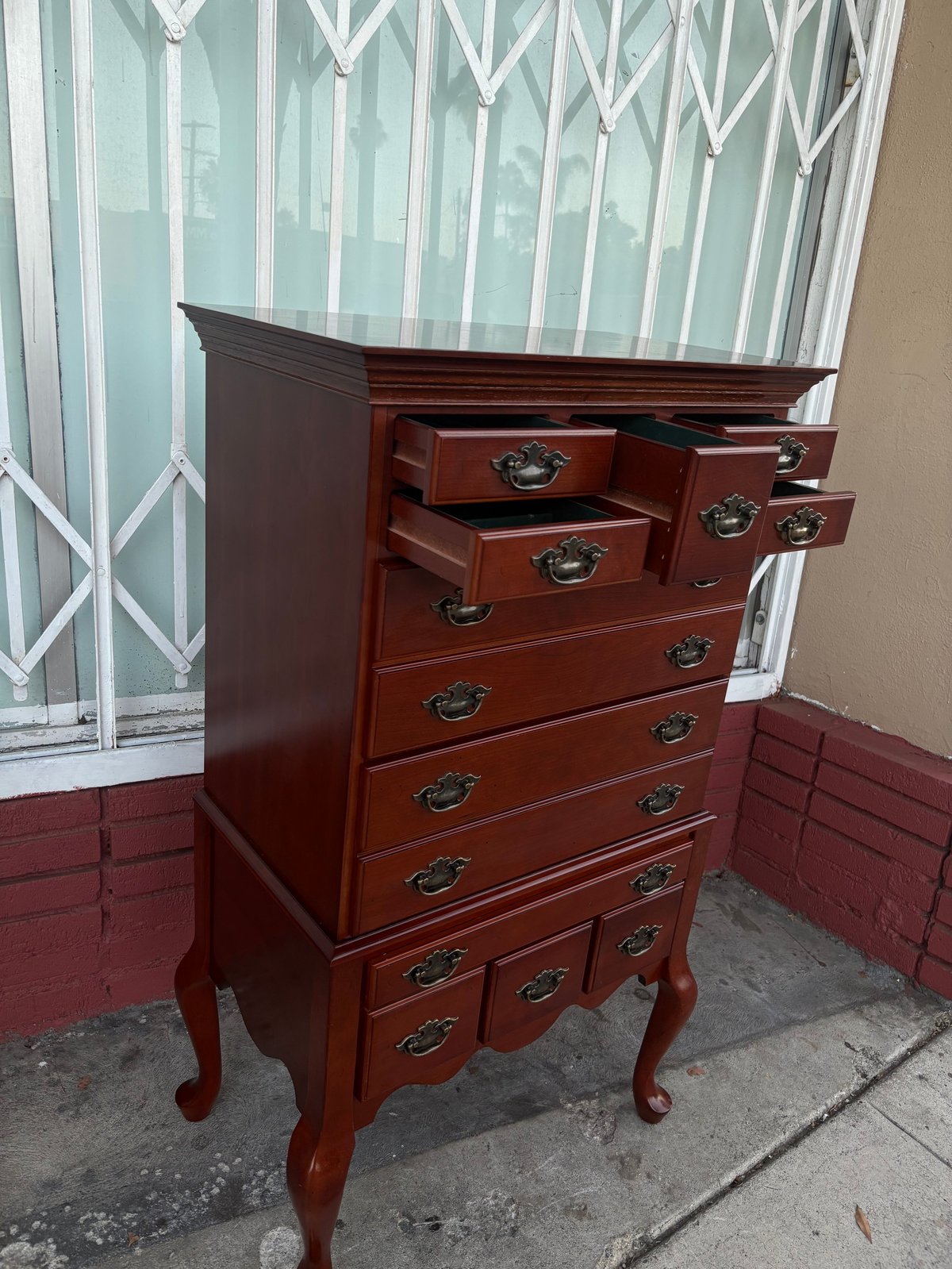 Dark red wooden chest of drawers with metal handles and curved legs on a patio, with a decorative door visible in the background