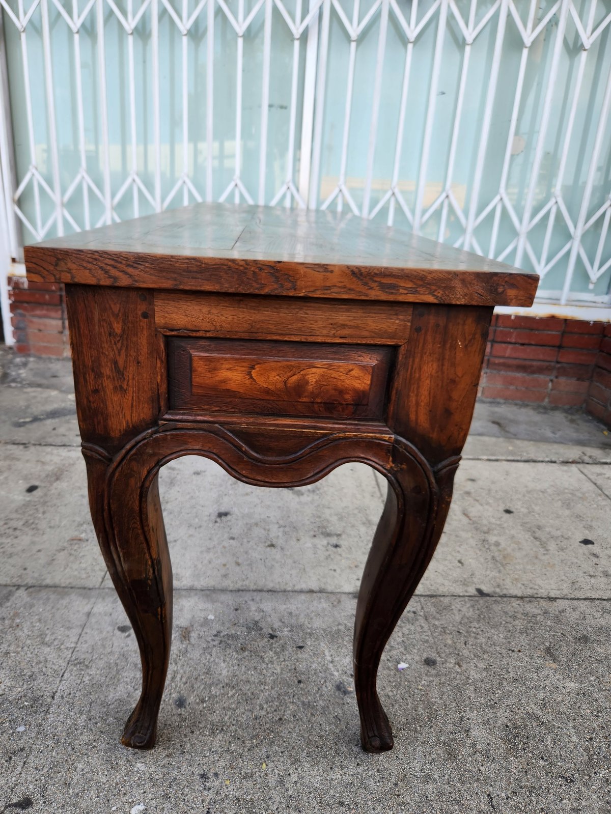 Antique wooden side table with ornate curved legs and inlaid drawer panel, displayed outdoors on pavement