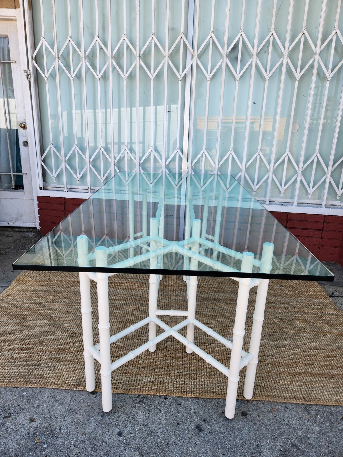 Modern glass dining table with white geometric base on tan rug, white accordion-style security gate visible in background