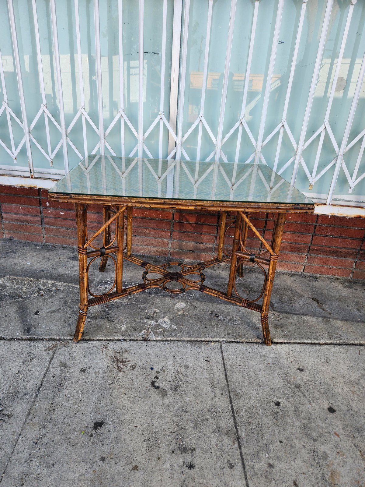 Antique bamboo side table with ornate metal frame on concrete patio, white accordion gate in background