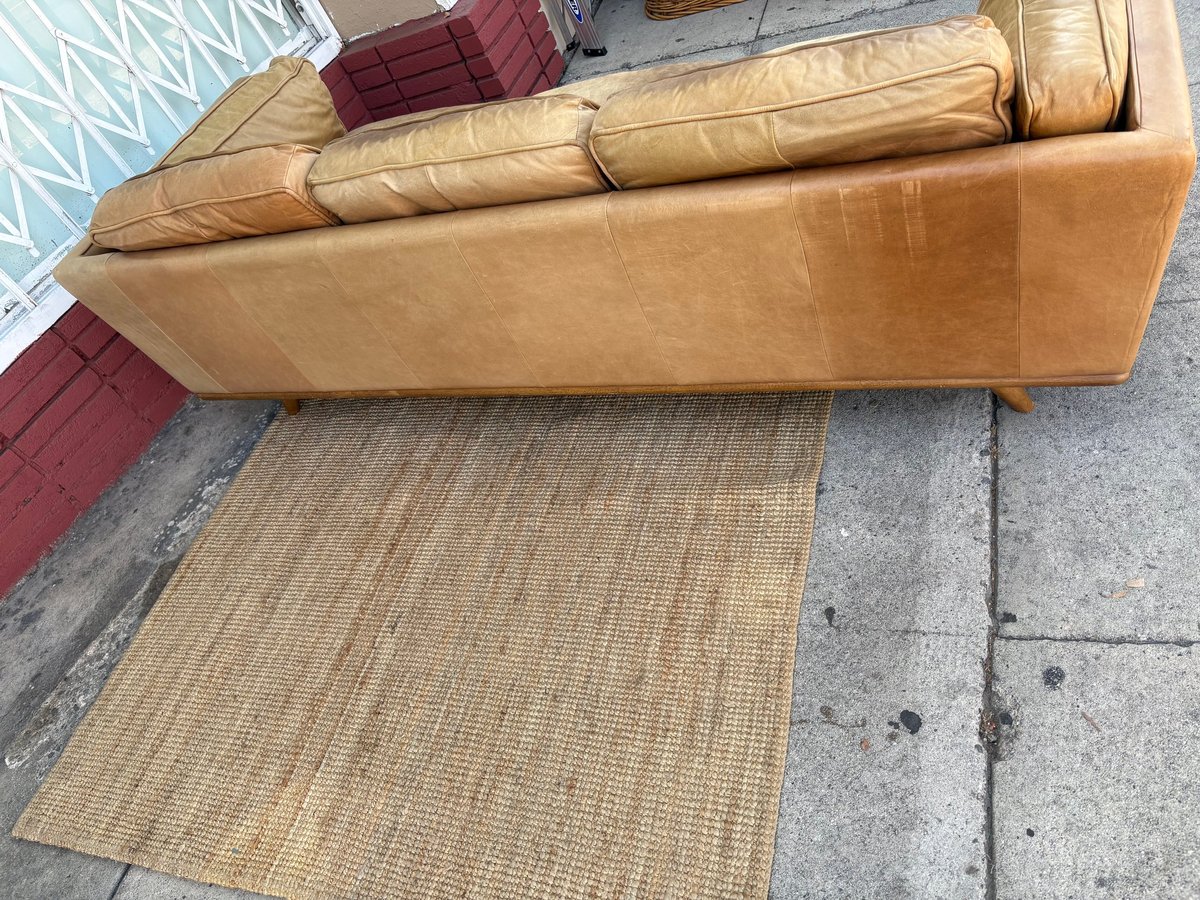 Tan leather sofa with pillows and a jute rug positioned on a sidewalk