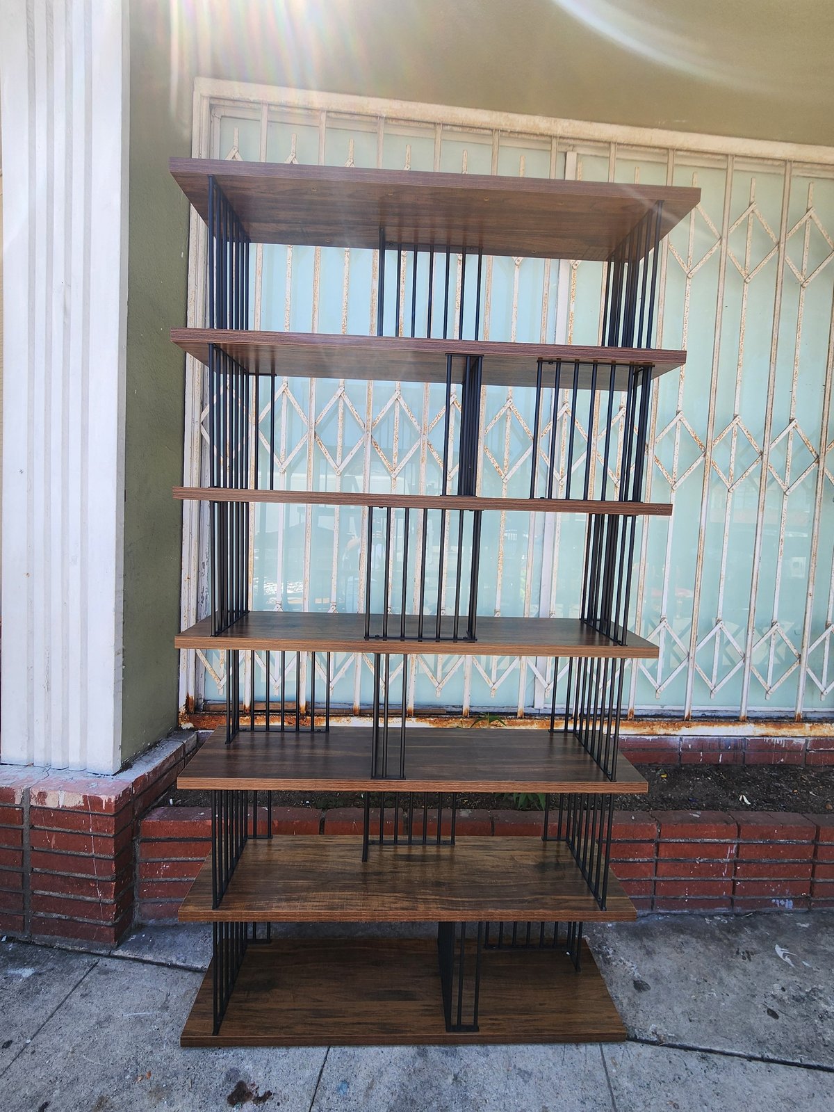 Tall wooden shelving unit with six tiers, metal frame supports, displayed outdoors against brick wall and window backdrop