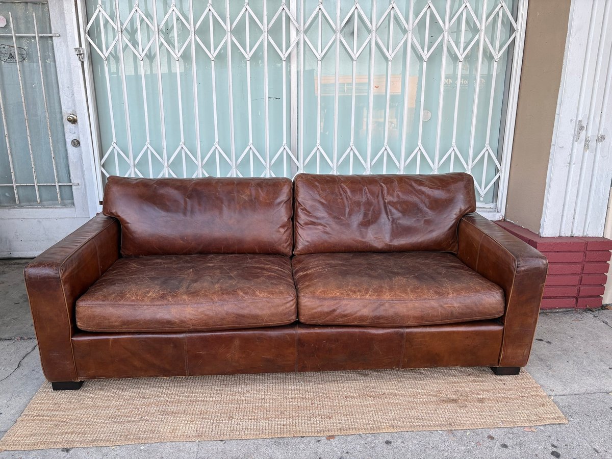 Brown leather two-seater sofa on beige rug in front of white metal gate