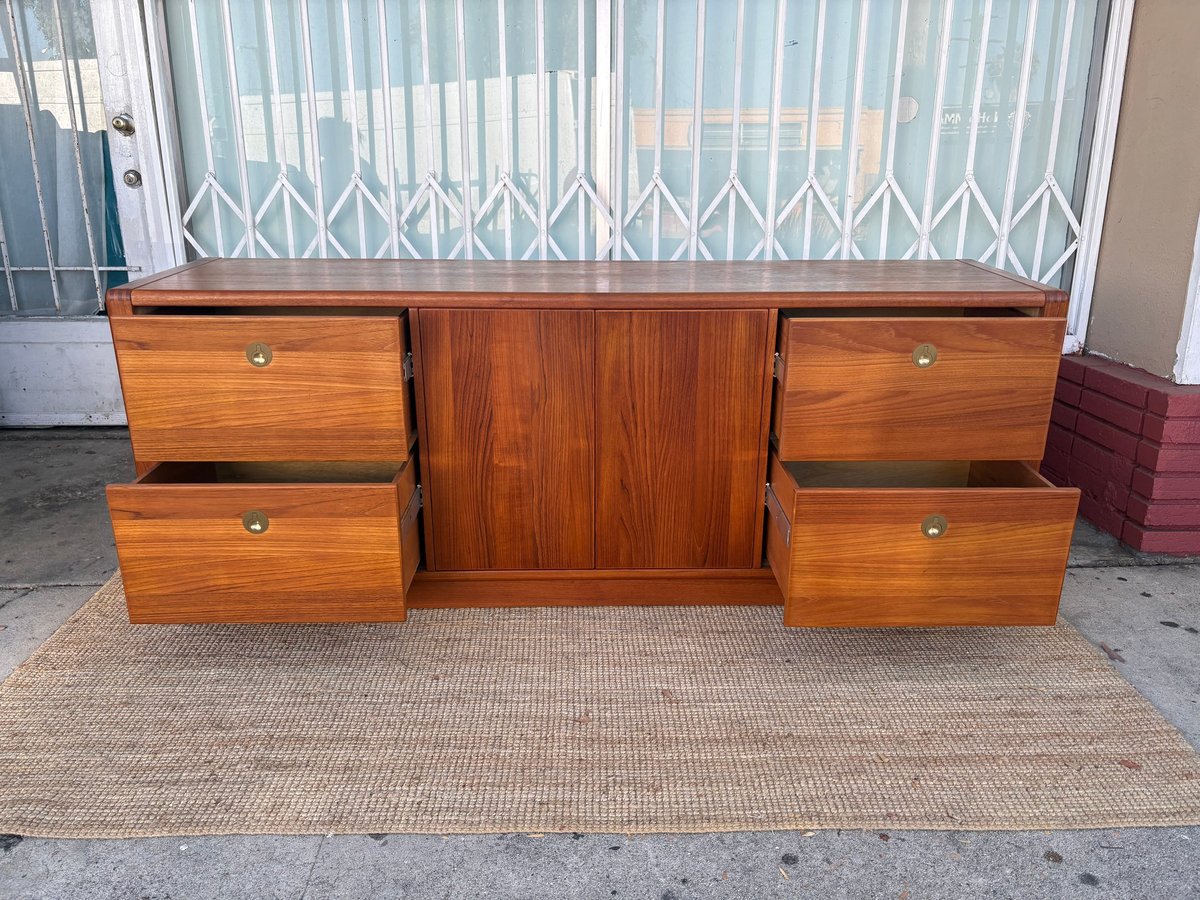 Mid-century wooden dresser with central cabinet and four side drawers positioned on outdoor mat against metal security gate