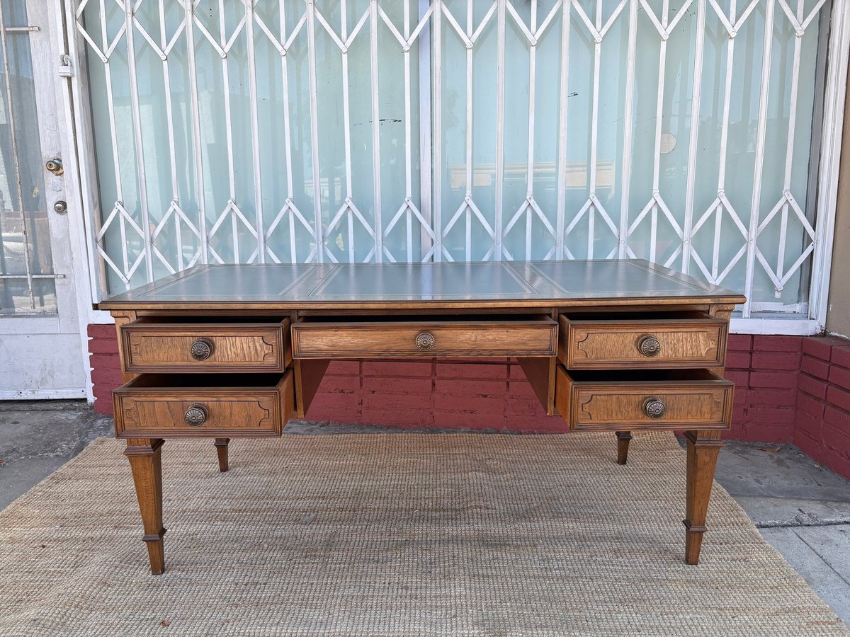 Wooden mid-century desk with four drawers and tapered legs displayed on a sidewalk.