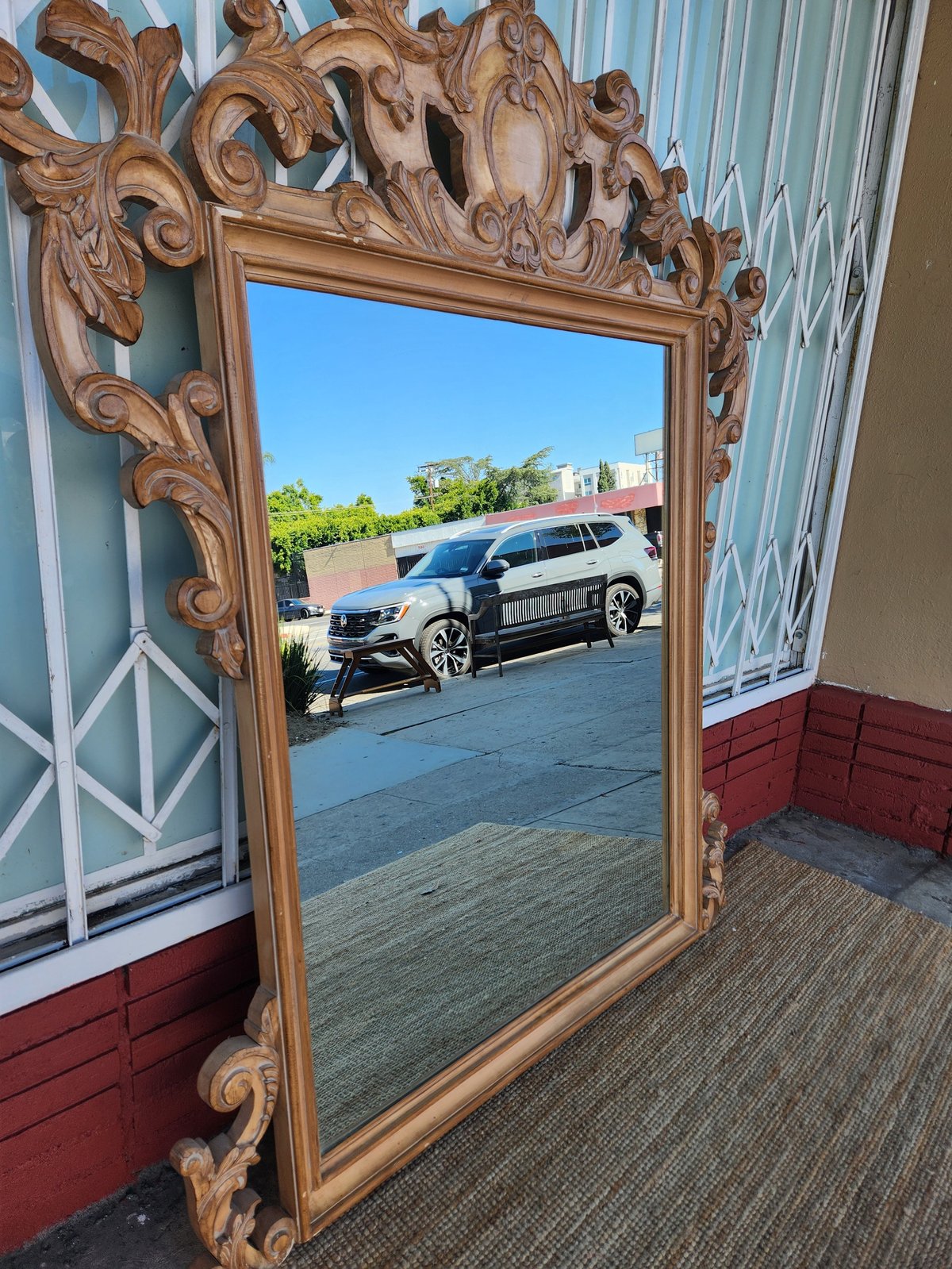 Ornate wooden mirror with carved baroque frame reflecting a black SUV parked outdoors