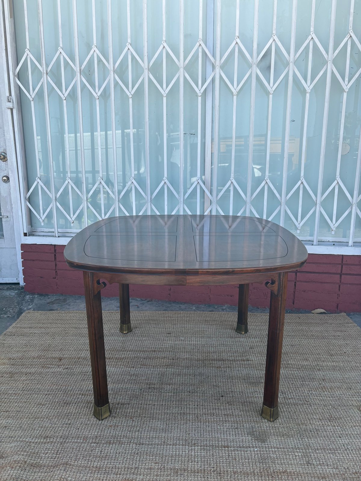 Oval wooden dining table with glass top on brick patio against metal security gate