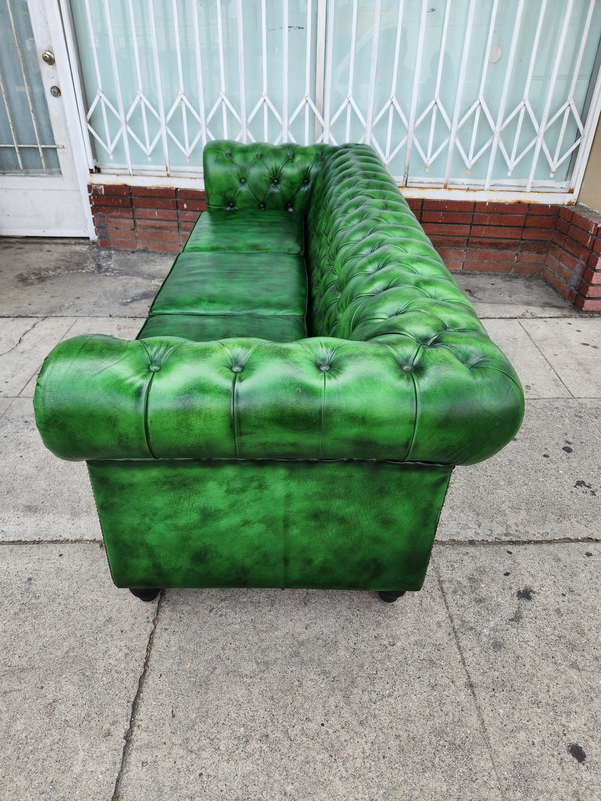 Green leather Chesterfield sofa with rolled arms and button tufting on outdoor concrete patio