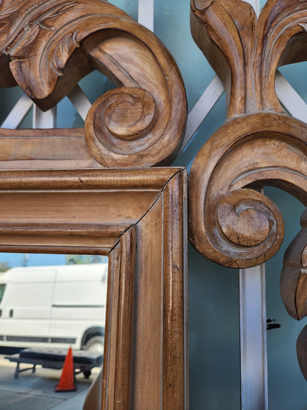 Ornate wooden mirror frame with carved scrolls and flourishes in warm brown finish