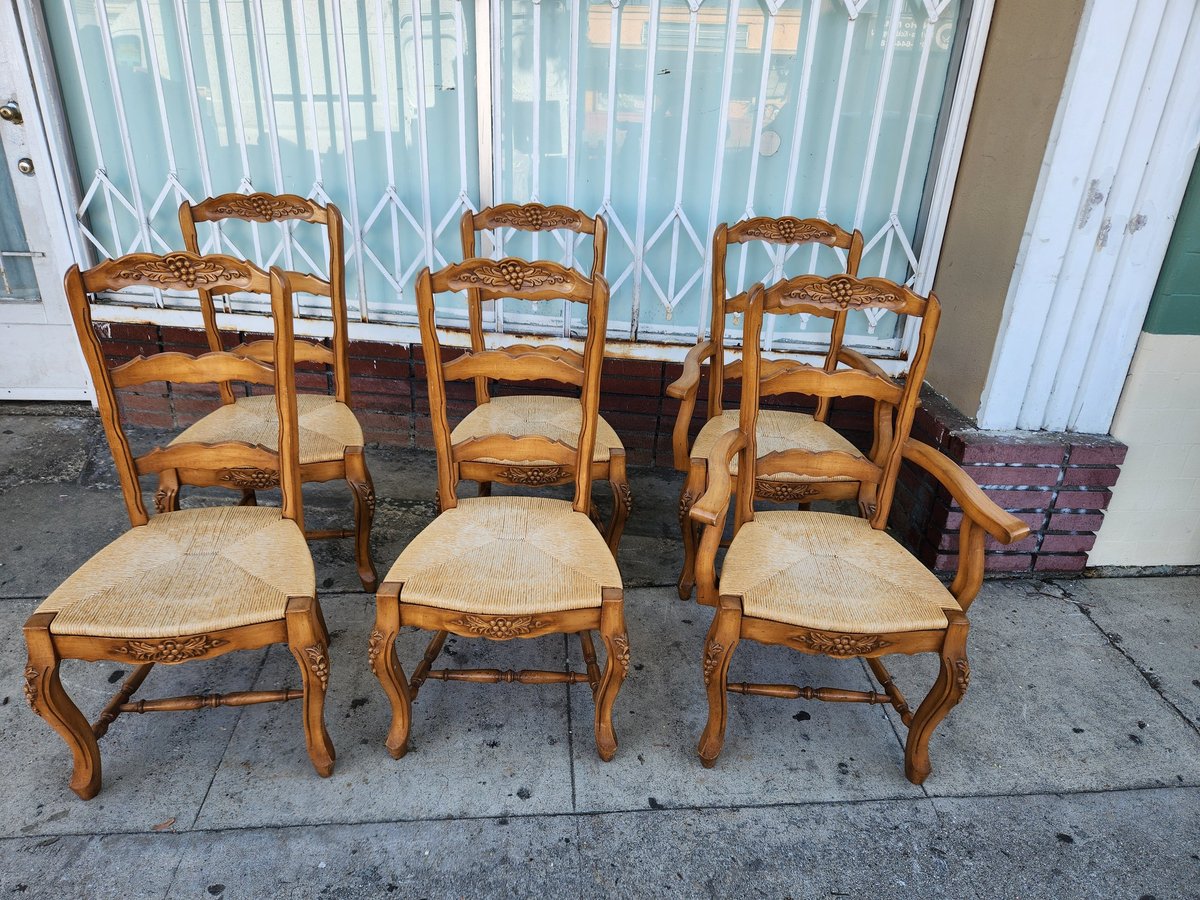 Six wooden dining chairs with woven rush seats arranged on a sidewalk in front of a building