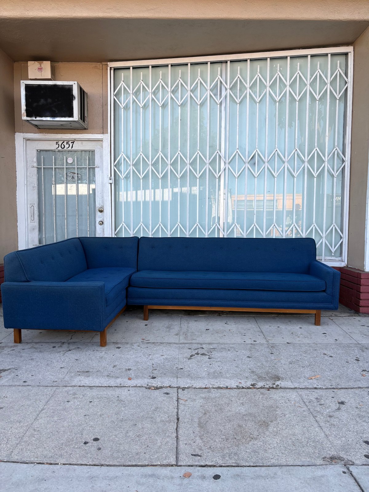 Modern blue sectional sofa on concrete floor in industrial warehouse space with metal security gate and microwave oven
