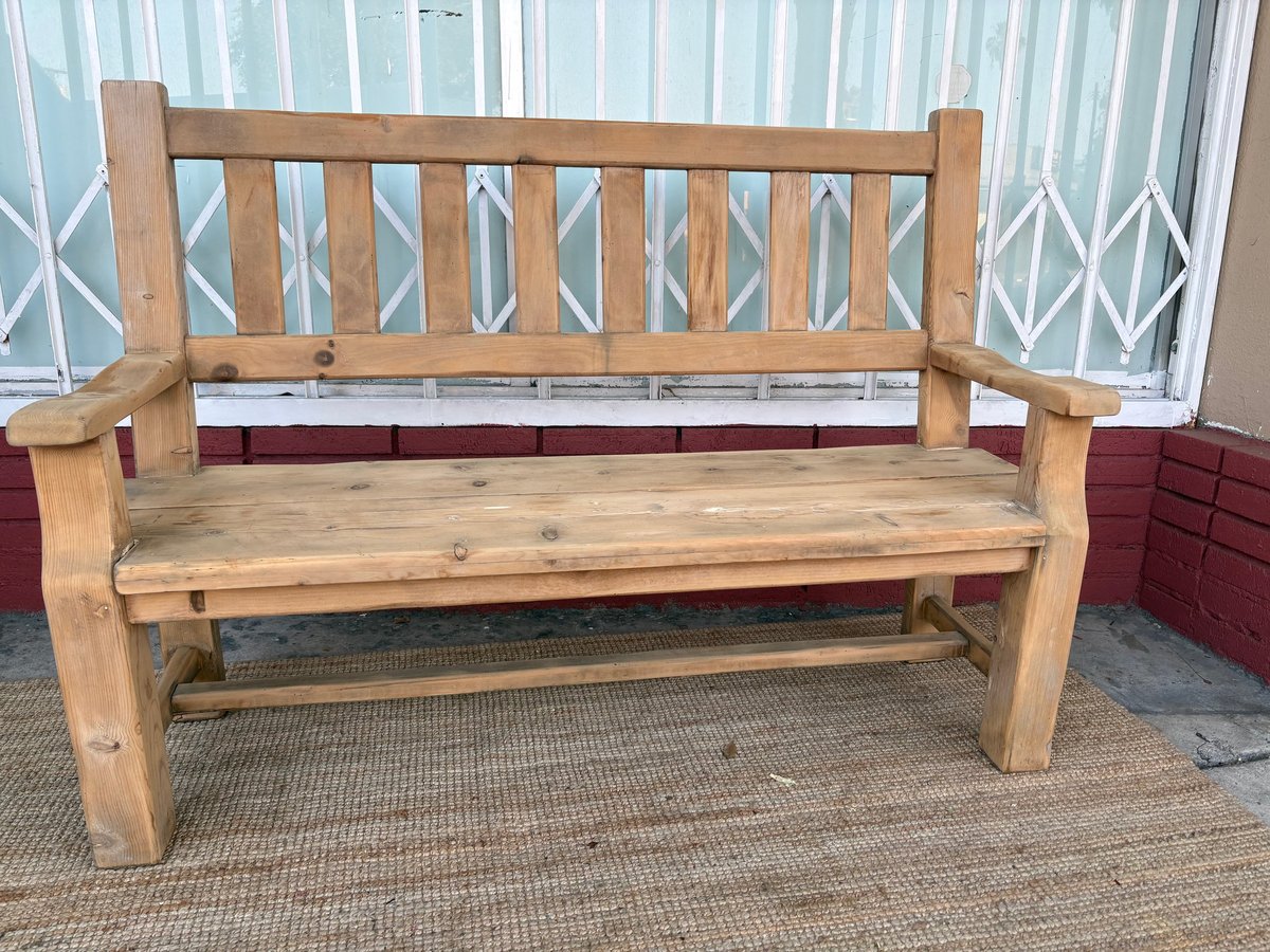 Wooden garden bench with vertical backrest slats on a paved patio area with white lattice fence