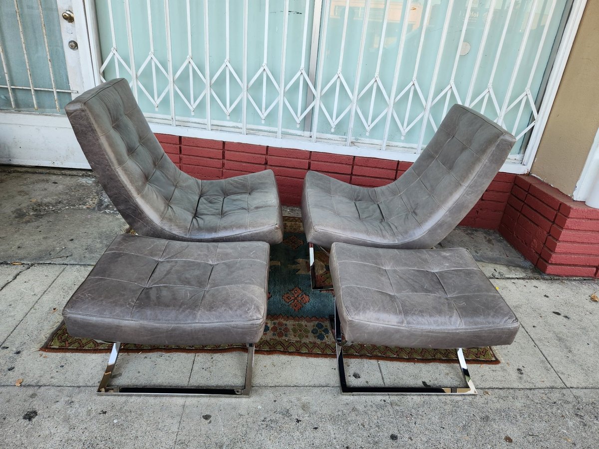 Pair of gray upholstered lounge chairs with matching ottomans arranged facing each other on concrete floor indoors