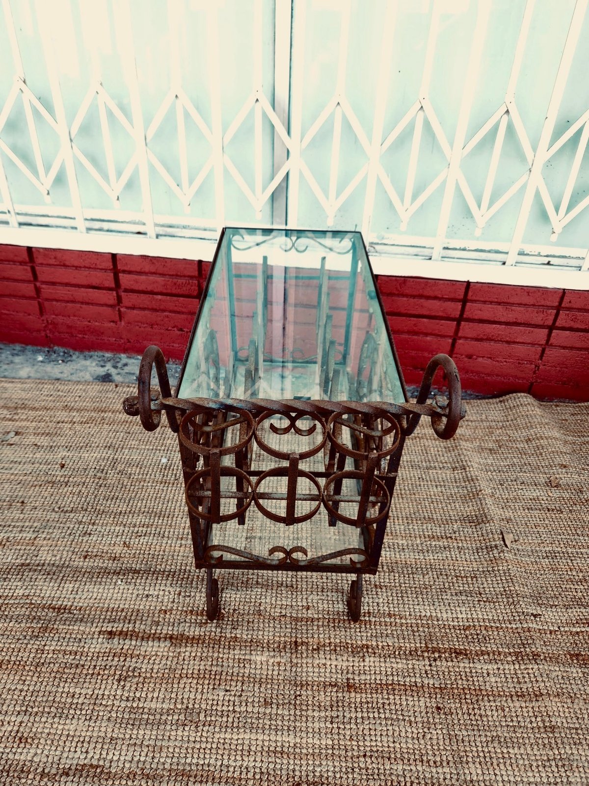 Ornate brown metal chair with glass top on concrete patio against red fence and white lattice wall