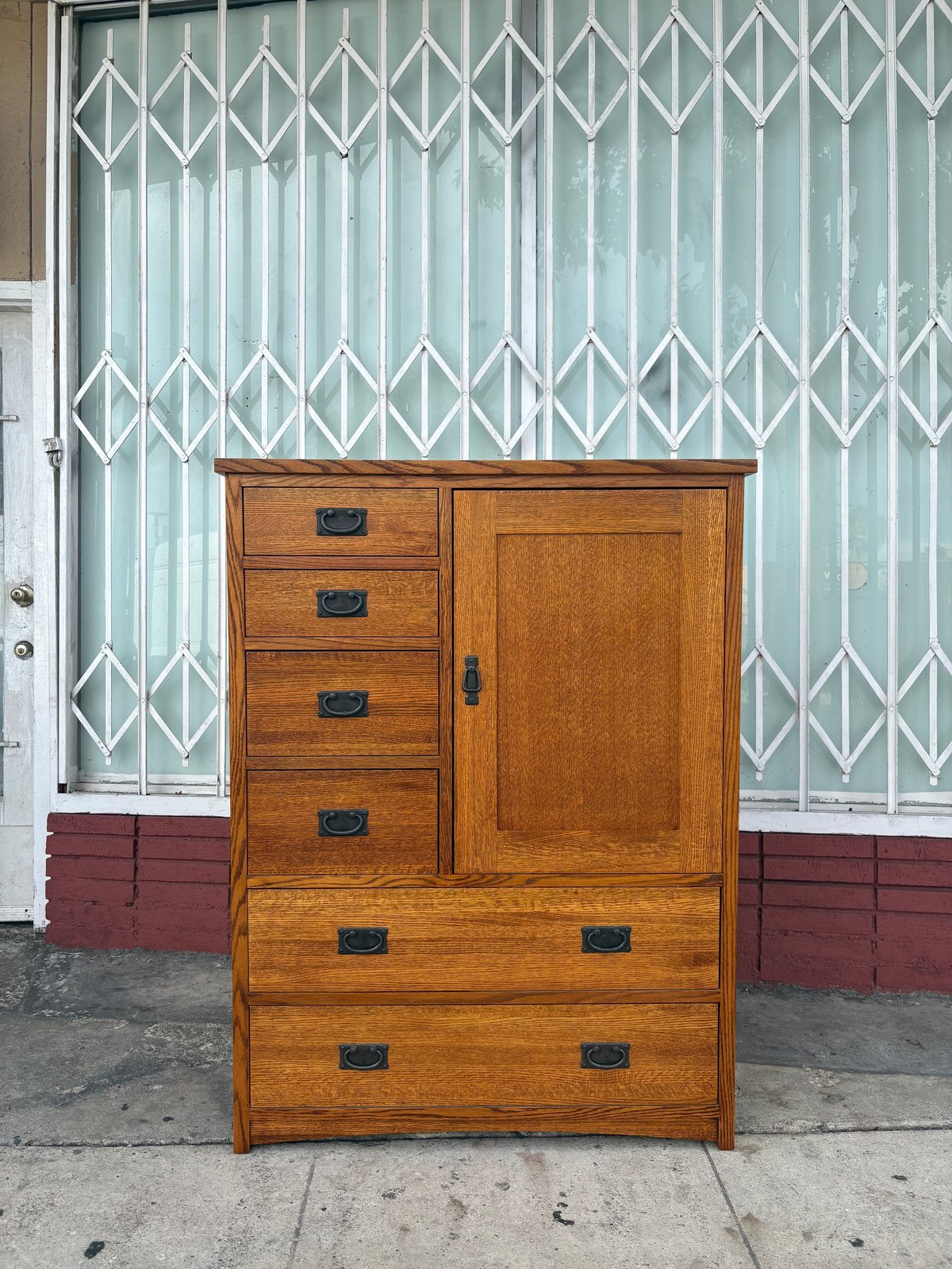 Wooden dresser with drawers and cabinet door against a metal security gate storefront