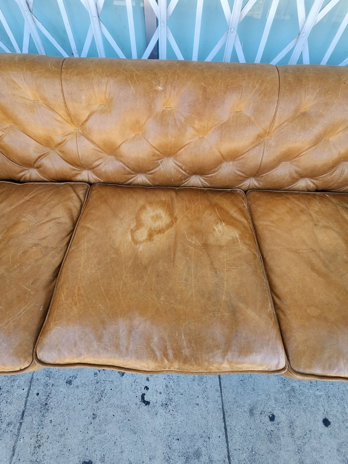Close-up of a tan leather sofa cushions showing quilted button tufting and wear marks against a blue geometric patterned wall
