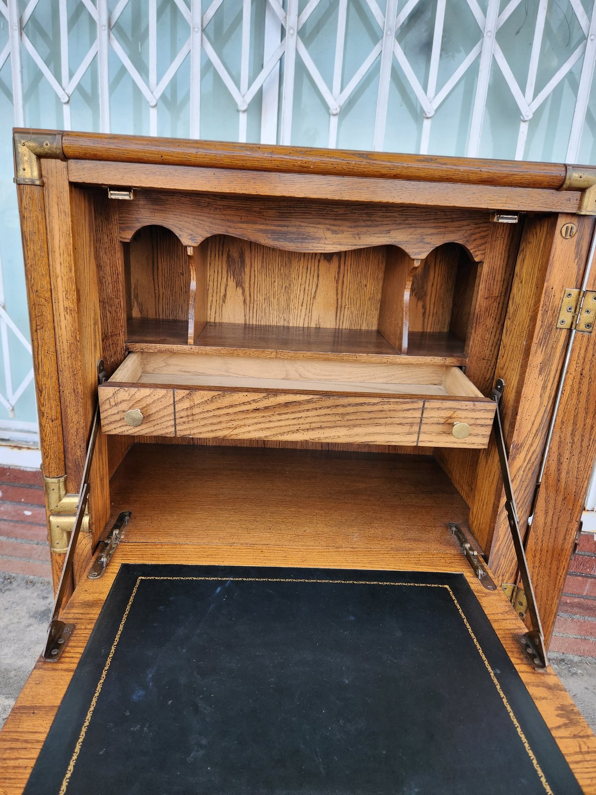 Open wooden cabinet with decorative arched top, shelves, and a black leather desktop insert on a white patterned background