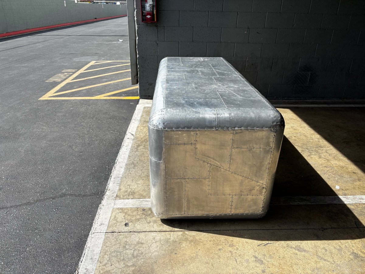 Metal cargo container wrapped in plastic sitting on a loading dock with yellow parking lines visible on asphalt