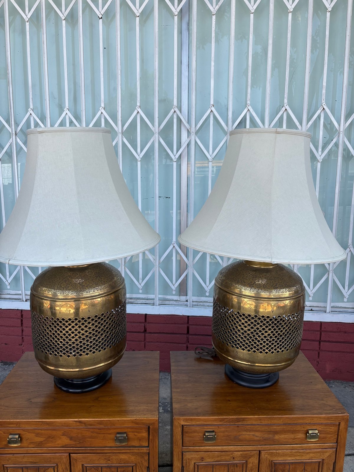 Pair of brass table lamps with white shades on wooden nightstands against a white geometric patterned wall