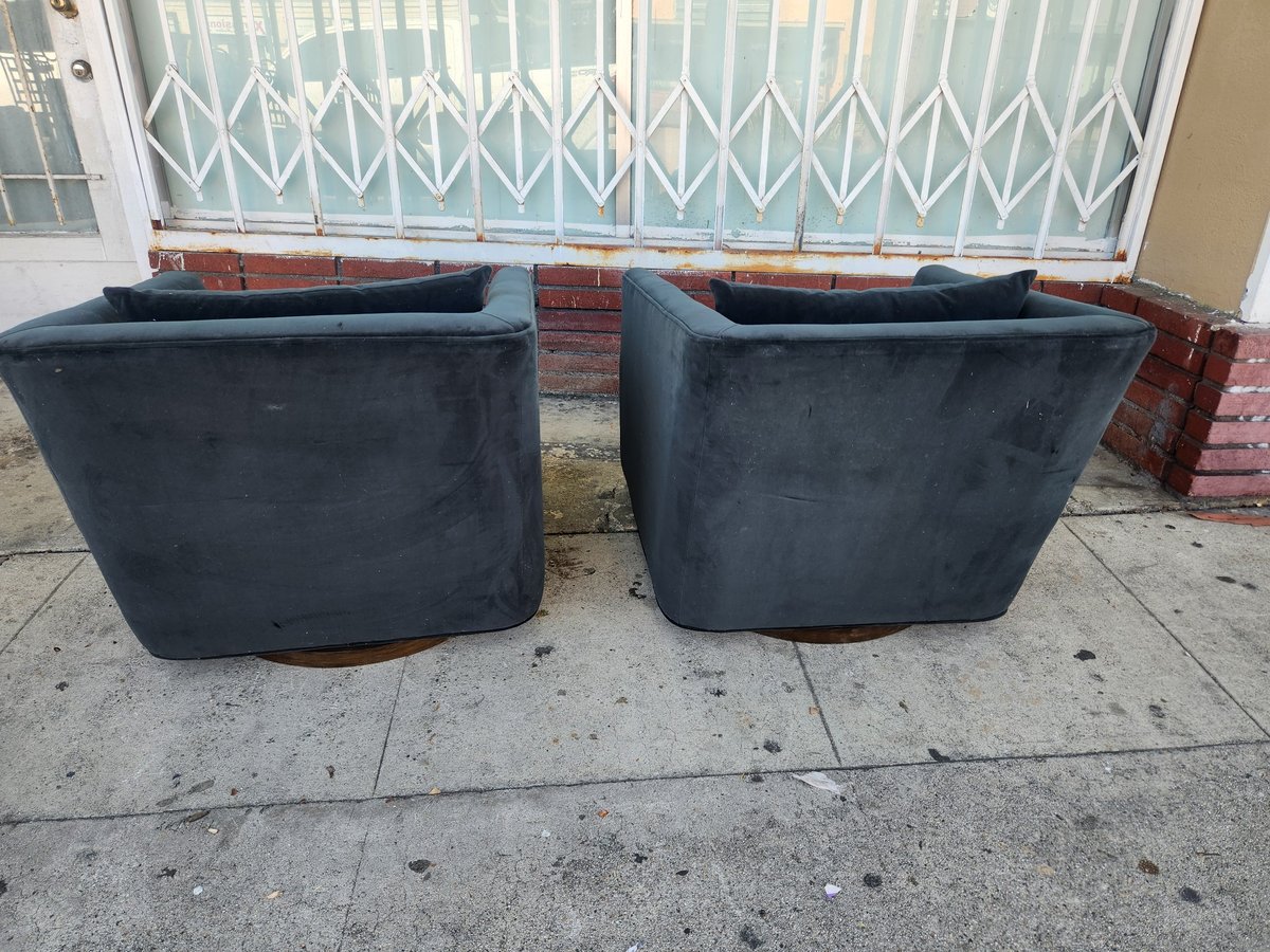 Two dark blue upholstered barrel chairs on concrete driveway in front of white metal gate and brick wall