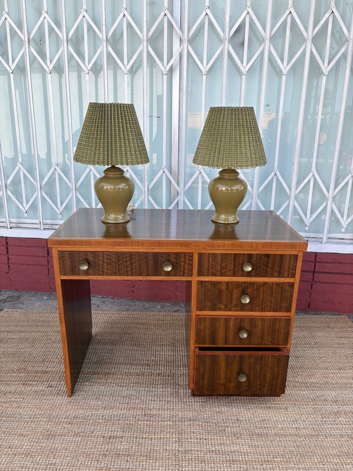 Mid-century modern wooden desk with drawers topped by two brass table lamps with pleated shades