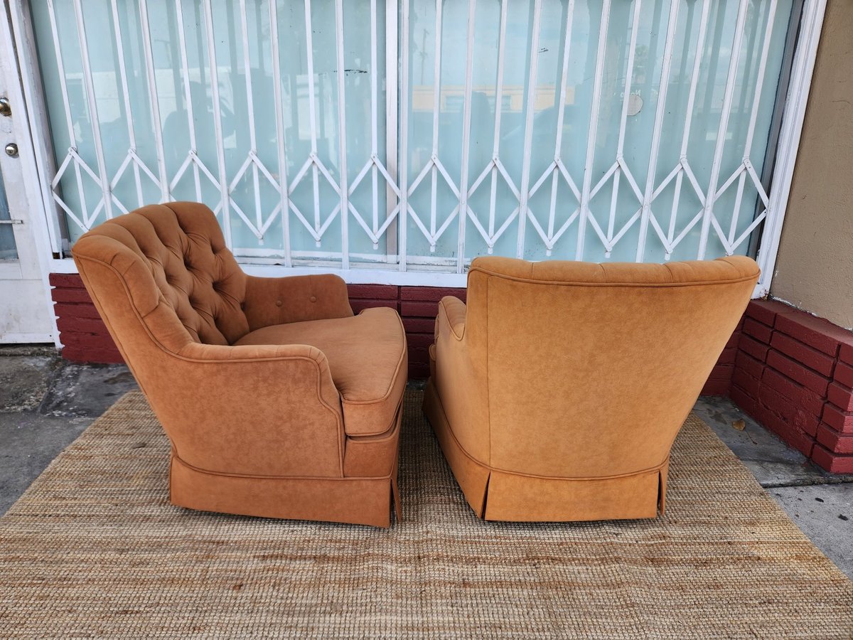 Two tan leather armchairs positioned on a beige rug, facing each other in front of a window with white geometric curtains