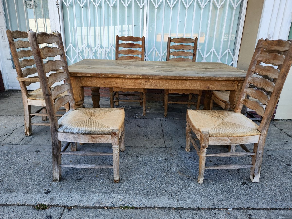 Rustic wooden dining set with a long table and six ladder-back chairs with woven rush seats displayed outdoors