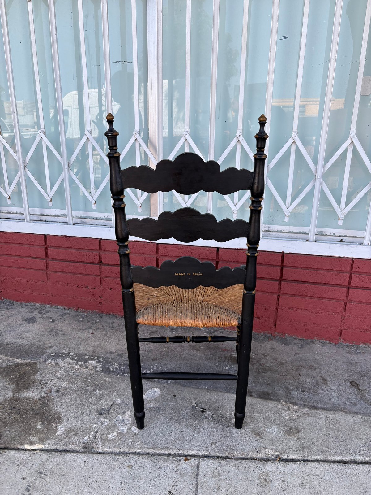 Black wooden chair with woven rush seat against a red and white building exterior