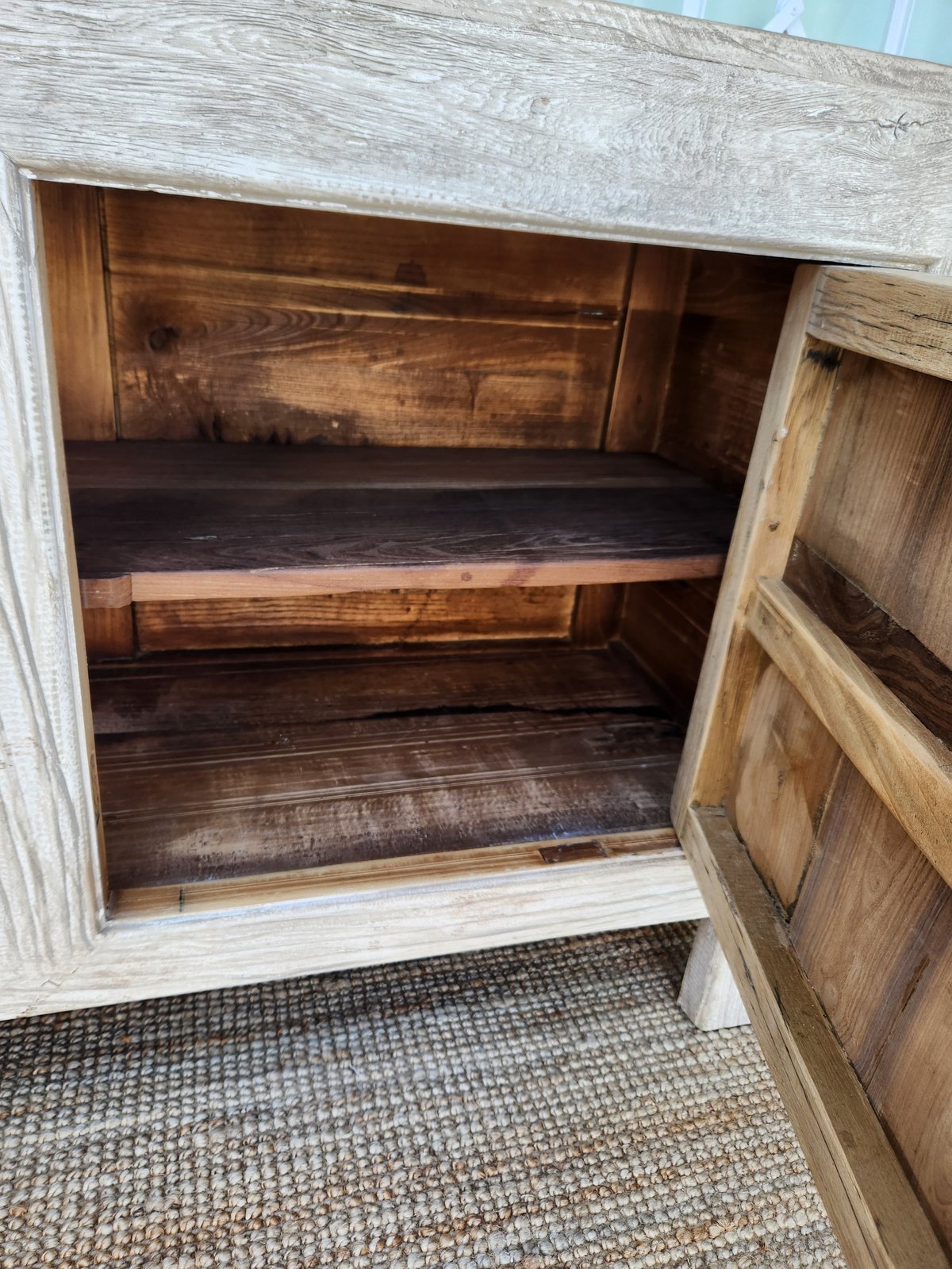 Empty wooden cabinet with open doors showing two dark wood shelves inside, displayed in bright sunlight