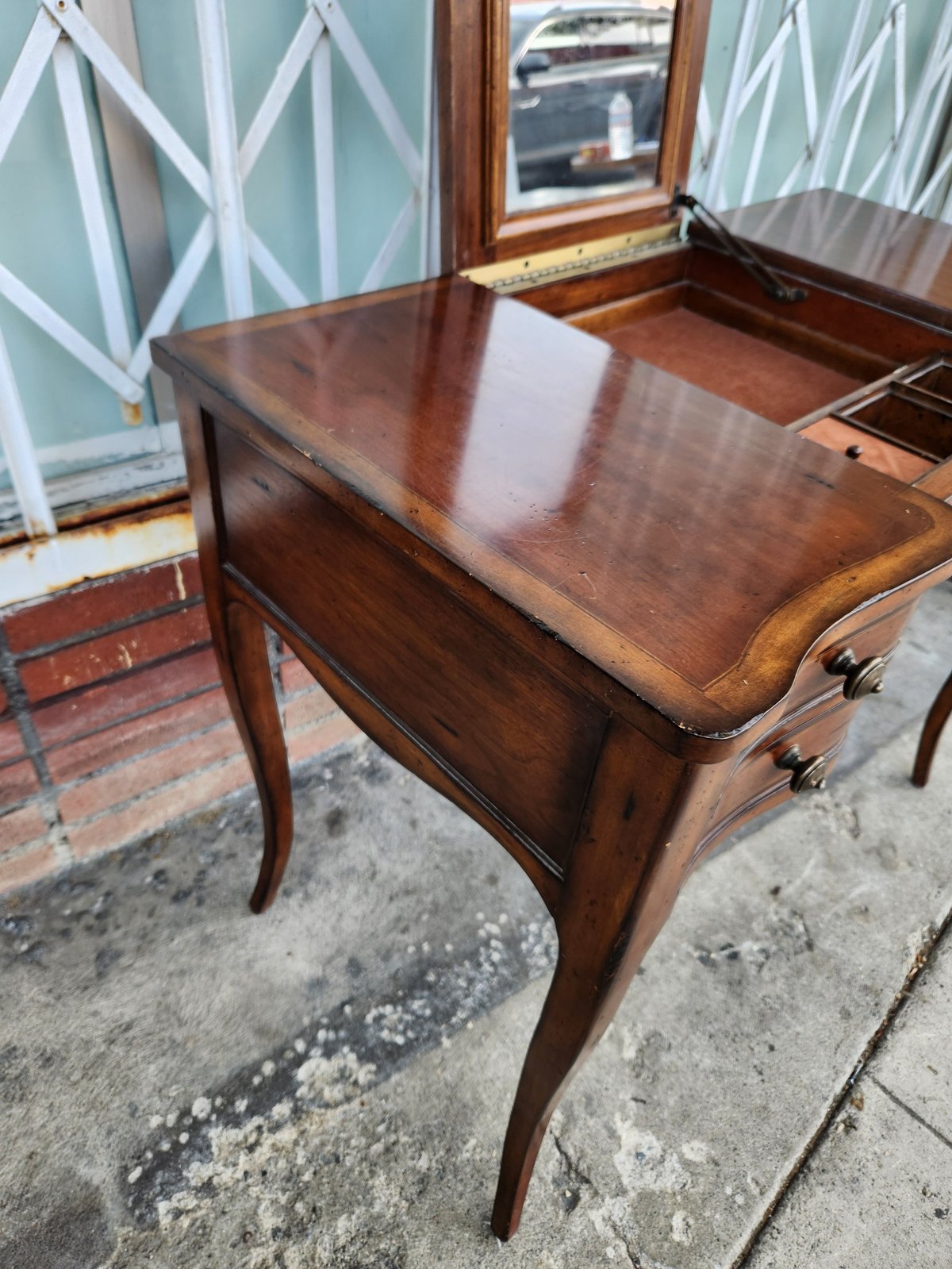 Antique wooden desk with two drawers and curved legs displayed outdoors, with pale blue fretwork panels visible in background