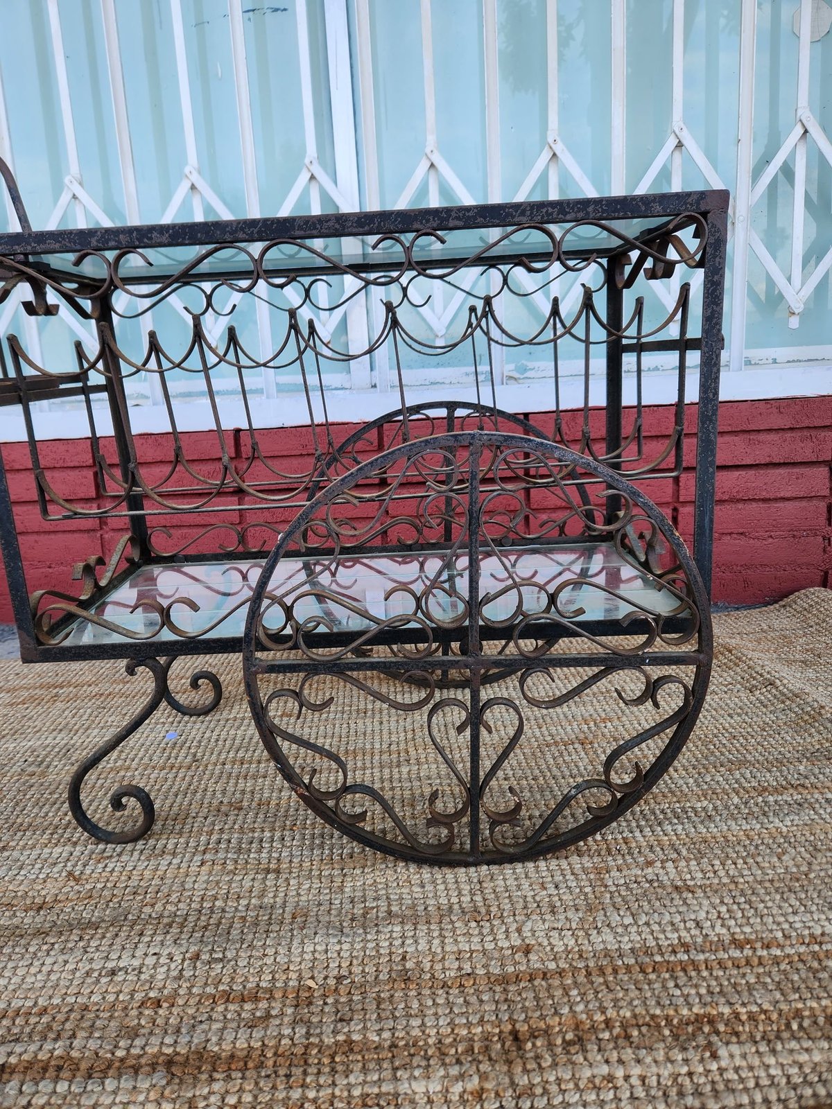 Ornate black wrought iron bench with decorative scrollwork against a red wall and white lattice fence