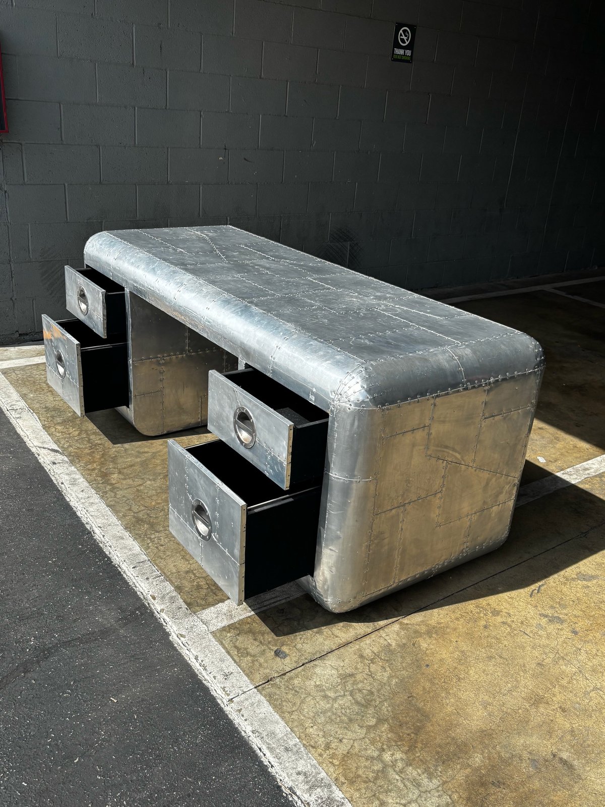 Metal storage bench with padded seat top and three open black drawers on sides in industrial garage setting