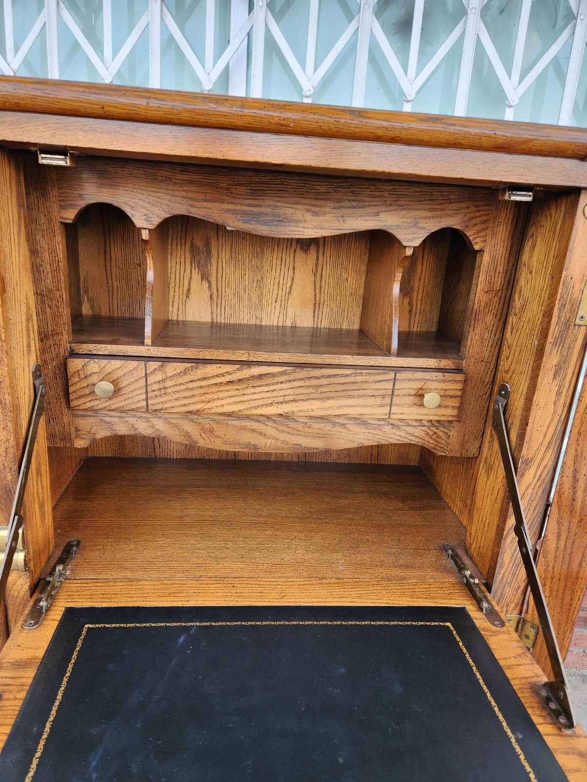 Open wooden cabinet with shelves and decorative arch details, showing interior storage space with blue patterned wallpaper above