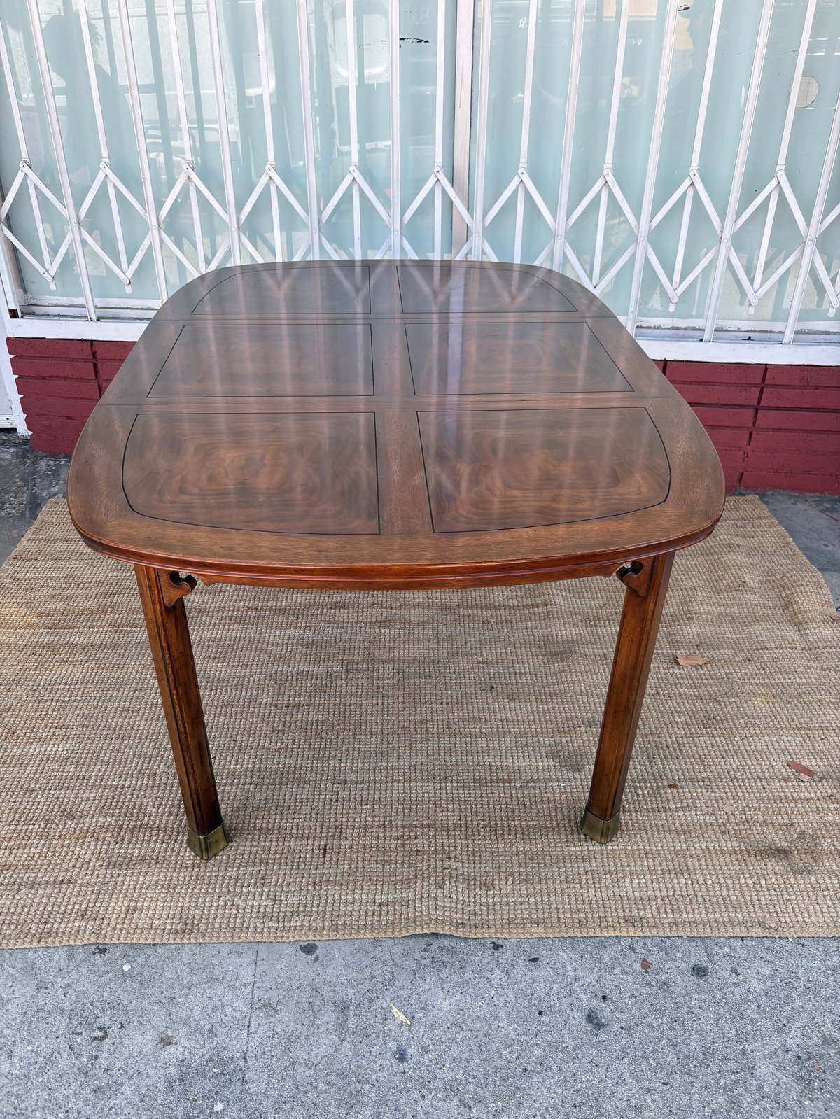 Wooden dining table with extension leaf on outdoor patio with metal gate and red wall in background