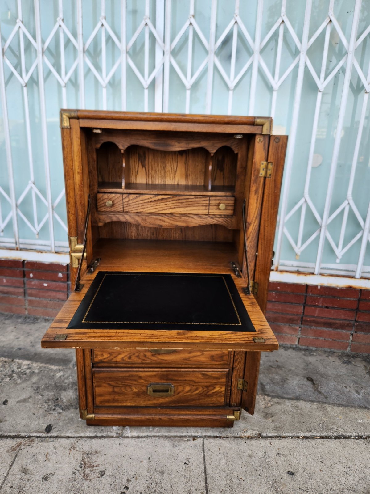 Vintage wooden cabinet with drop-down desk front and open upper shelves, displayed on a sidewalk