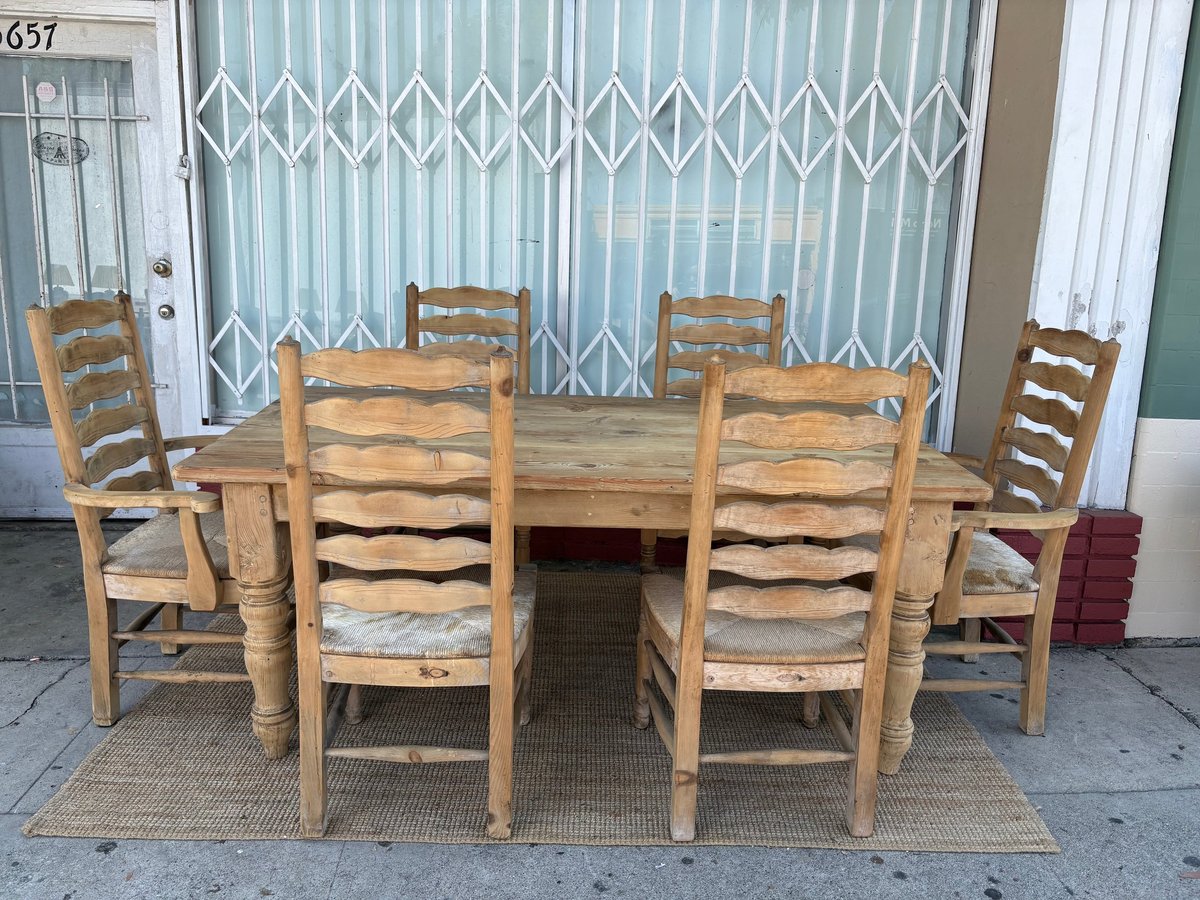 Wooden dining table set with six ladder-back chairs arranged on a patio in front of a white accordion gate door