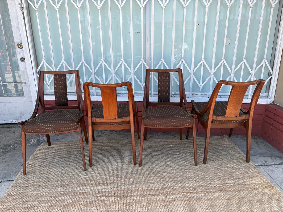 Four mid-century wooden dining chairs with upholstered seats arranged on a beige rug against a garage door background