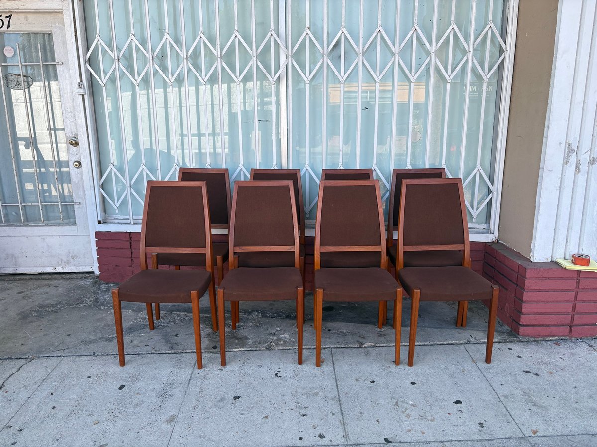 Four brown upholstered dining chairs arranged in a row on a sidewalk in front of a metal gate