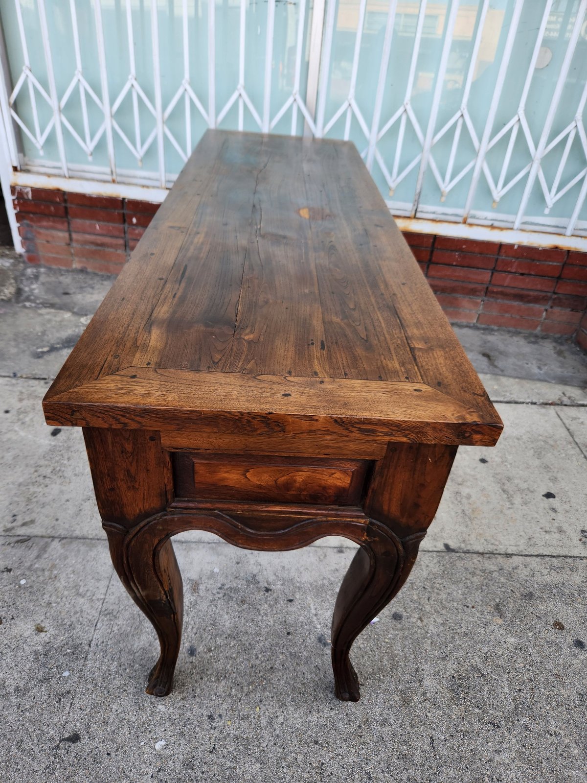 Antique wooden side table with ornate curved legs and drawer, displayed outdoors on concrete