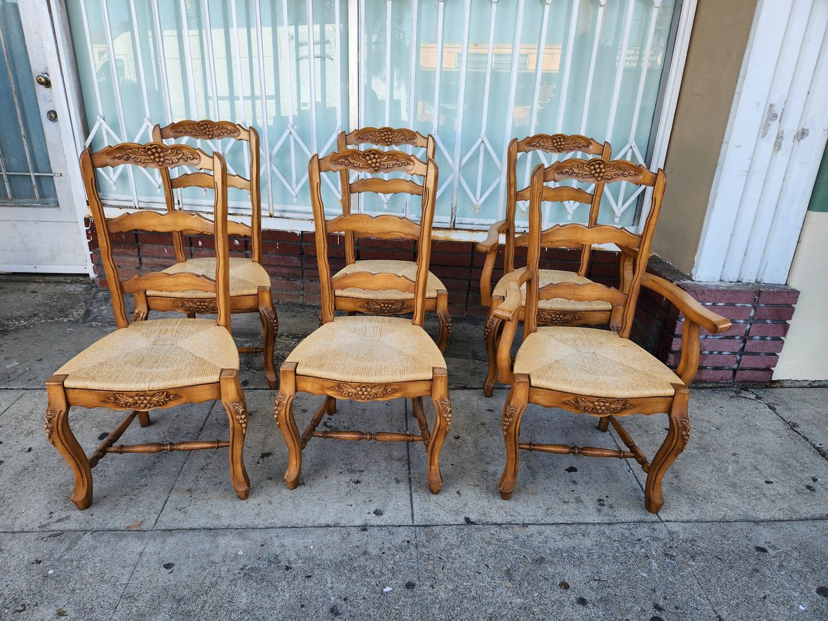 Three ornate wooden dining chairs with cream-colored woven seats displayed outdoors on pavement