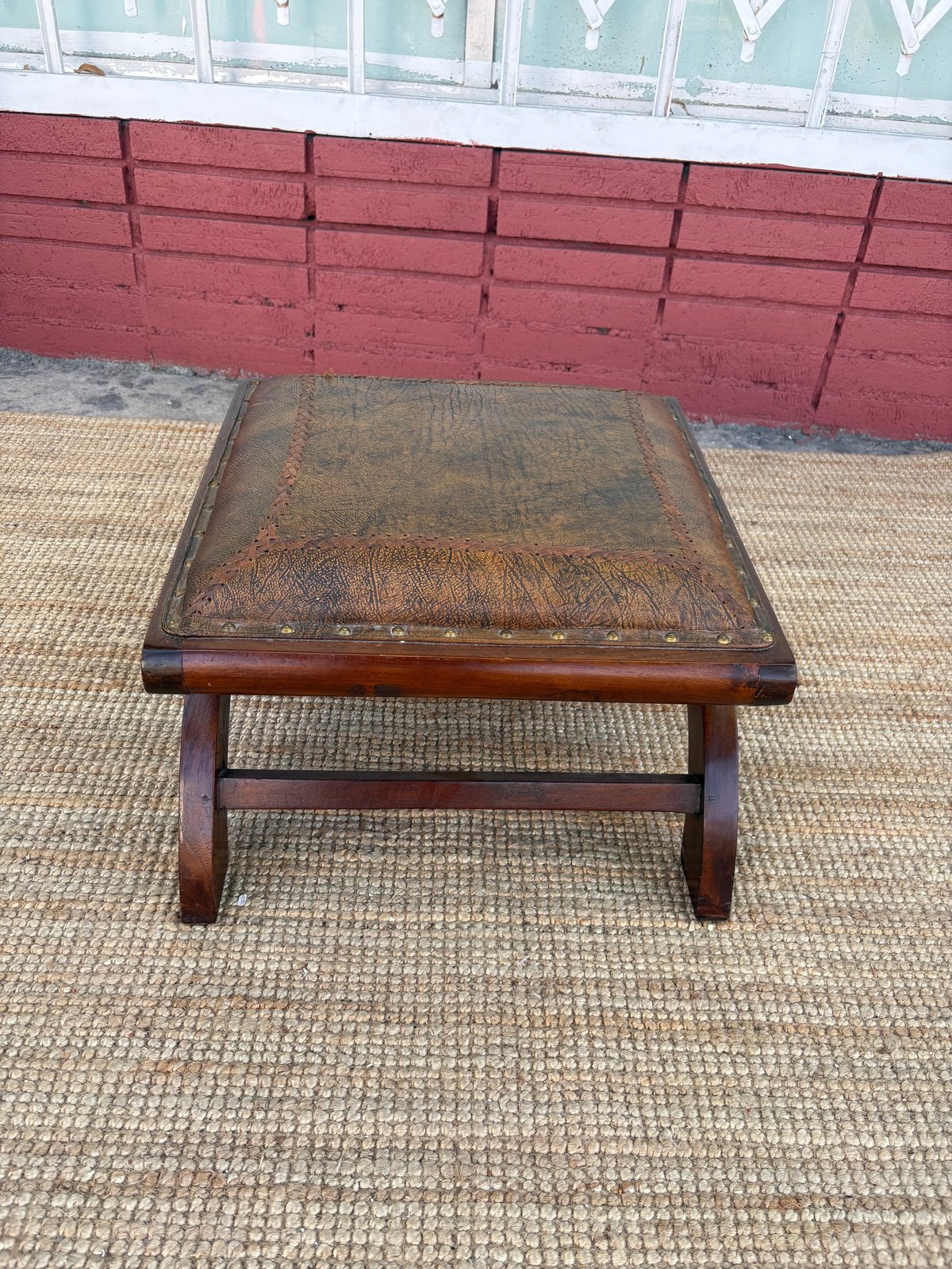 Vintage wooden bench with worn brown leather seat top outdoors on pavement against red wooden wall